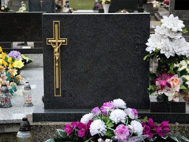 Lápida de piedra con cruz dorada y flores en un cementerio de San Cibrao das Viñas